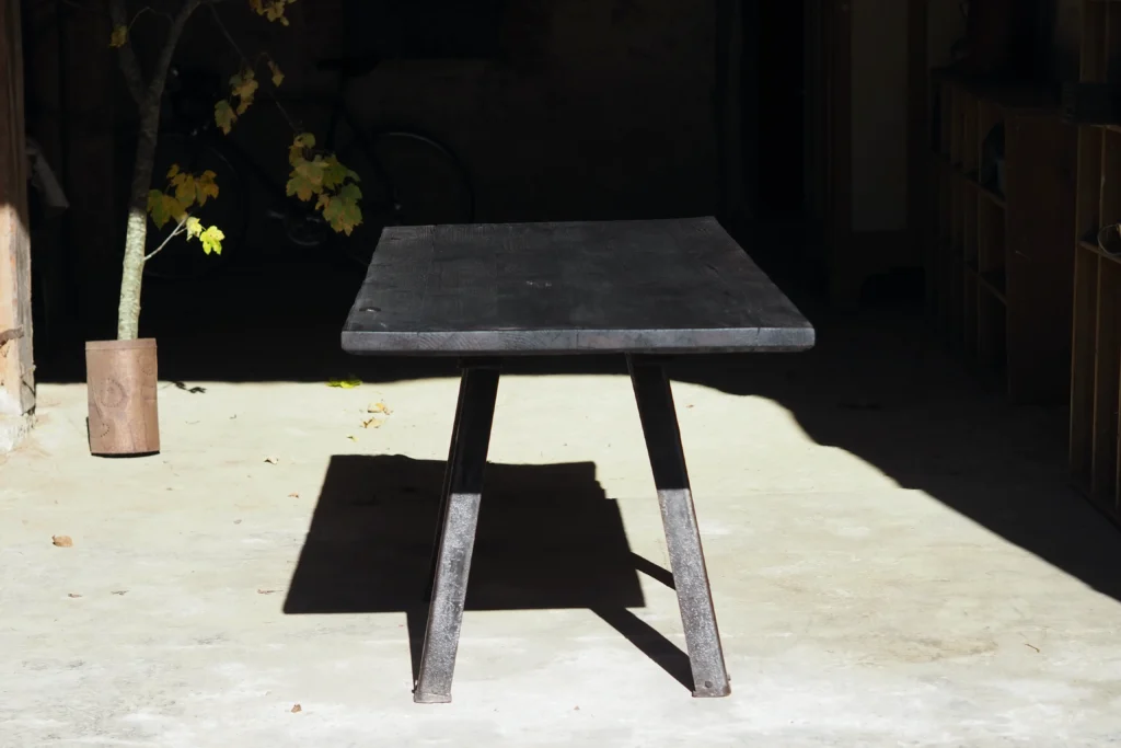 das Bild zeigt einen schwarz geköhlten Tisch in einer alten Scheune